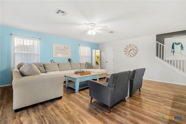 living room featuring stairway, visible vents, ceiling fan, baseboards, and wood finished floors