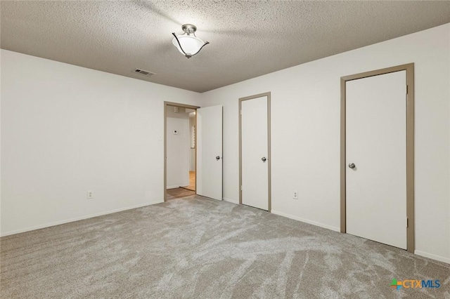 unfurnished bedroom with carpet, visible vents, a textured ceiling, and baseboards