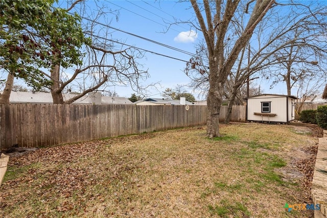 view of yard with a fenced backyard, a storage unit, and an outbuilding