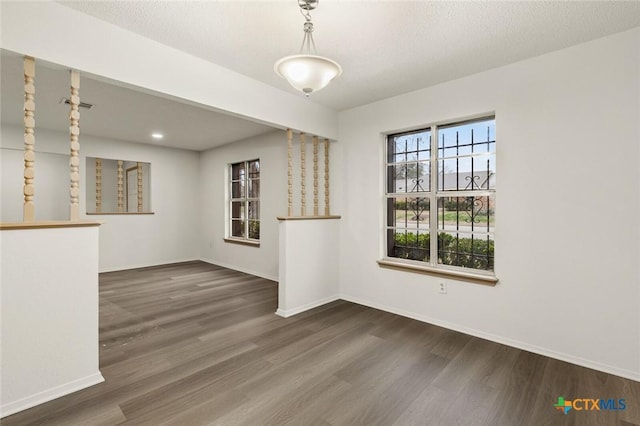 spare room with a textured ceiling, wood finished floors, visible vents, and baseboards