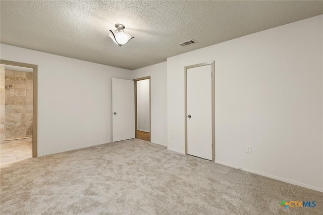 unfurnished bedroom with a textured ceiling, carpet flooring, visible vents, and ensuite bathroom