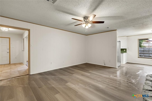 spare room featuring a textured ceiling, ceiling fan, wood finished floors, visible vents, and ornamental molding