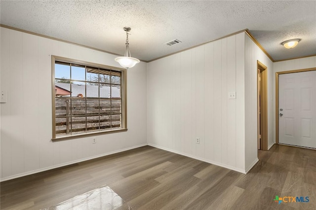 unfurnished dining area featuring crown molding, visible vents, a textured ceiling, wood finished floors, and baseboards