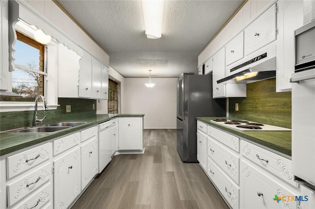 kitchen with dark countertops, a sink, a peninsula, white appliances, and under cabinet range hood