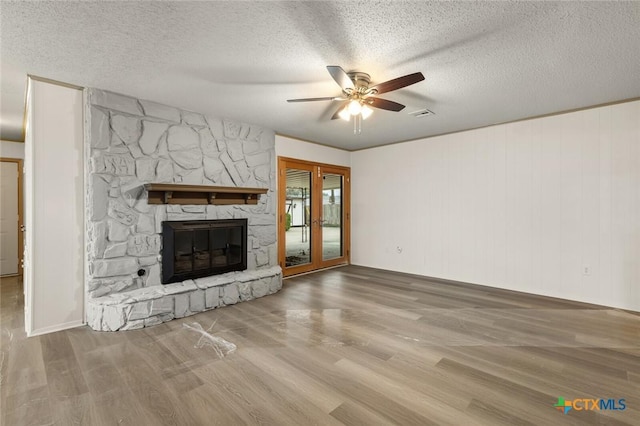 unfurnished living room featuring ceiling fan, a stone fireplace, a textured ceiling, and wood finished floors