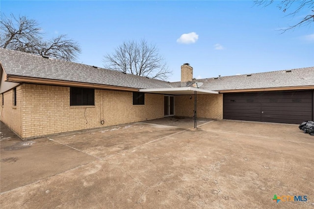 rear view of property with a garage, concrete driveway, brick siding, and a chimney