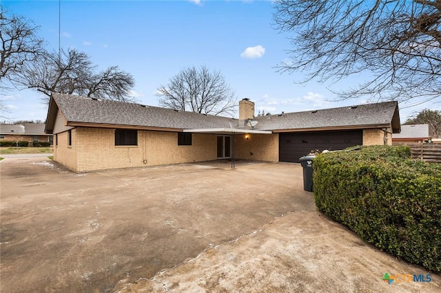 ranch-style home with an attached garage, a chimney, concrete driveway, and brick siding