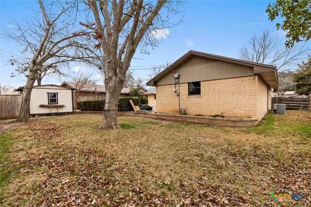 view of home's exterior with an outbuilding, brick siding, central air condition unit, a lawn, and fence