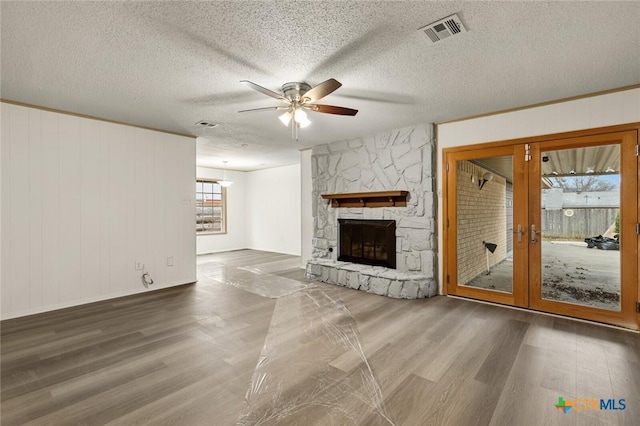 unfurnished living room featuring visible vents, a ceiling fan, wood finished floors, a textured ceiling, and a fireplace