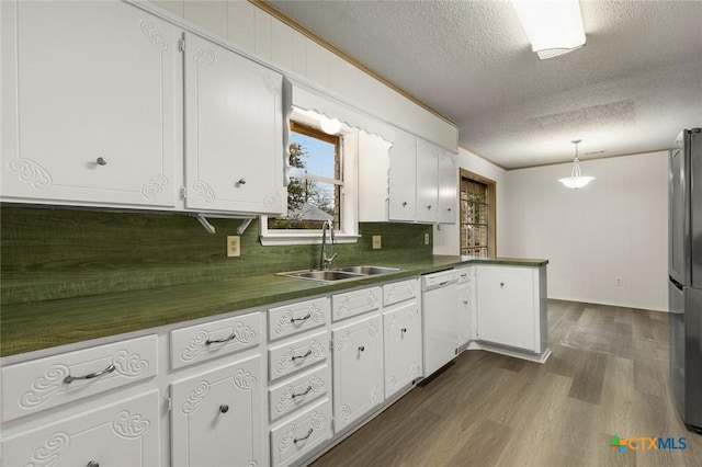 kitchen featuring a peninsula, a sink, dishwasher, dark countertops, and dark wood finished floors