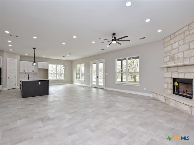 unfurnished living room with a stone fireplace, a wealth of natural light, ceiling fan, and sink