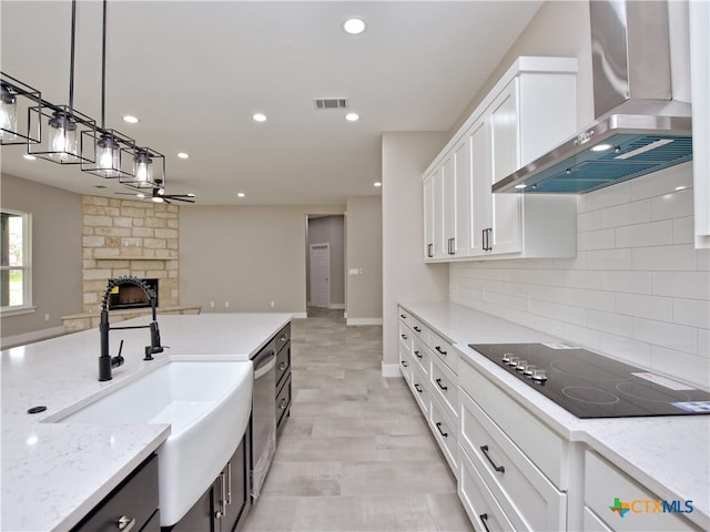 kitchen with black electric cooktop, white cabinetry, light stone counters, wall chimney range hood, and pendant lighting