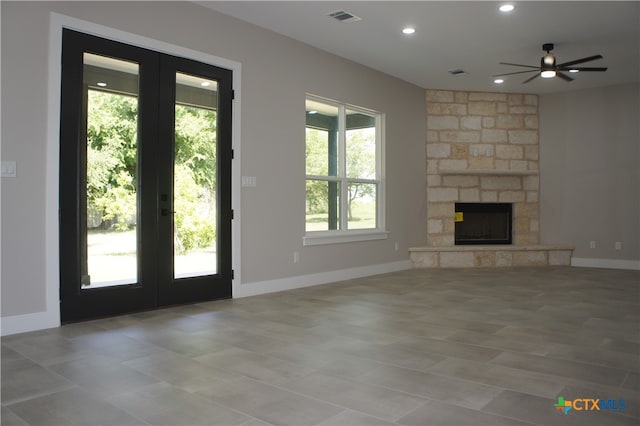 unfurnished living room with a stone fireplace, french doors, and ceiling fan