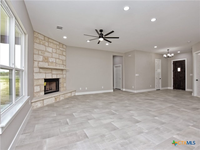 unfurnished living room featuring a stone fireplace and ceiling fan with notable chandelier