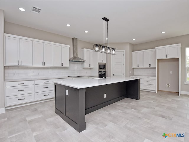 kitchen featuring white cabinets, wall chimney exhaust hood, a center island with sink, and stainless steel microwave