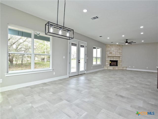 unfurnished living room with ceiling fan, a stone fireplace, and plenty of natural light