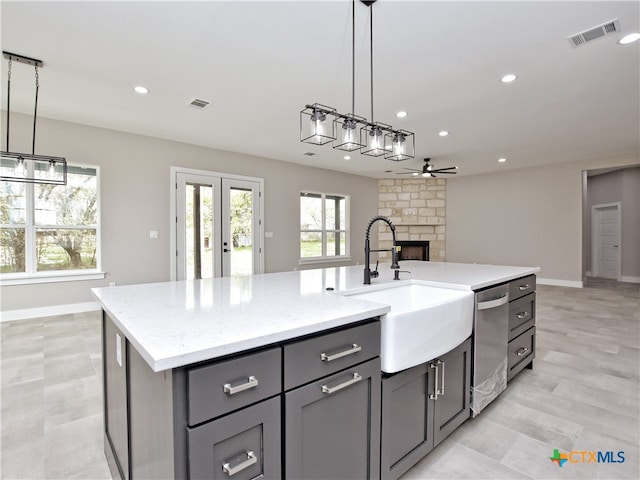 kitchen with sink, an island with sink, stainless steel dishwasher, pendant lighting, and a fireplace