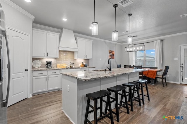 730 Eagle Pass Dr, Salado, TX 76571 - kitchen with a kitchen island with sink, white cabinets, hanging light fixtures, and custom range hood