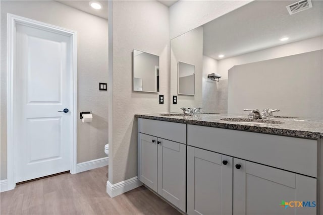 bathroom featuring a sink, toilet, visible vents, baseboards, and wood finished floors