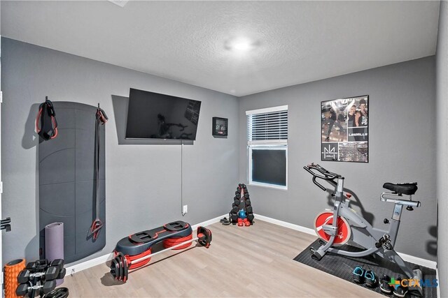 exercise area with a textured ceiling, wood finished floors, and baseboards