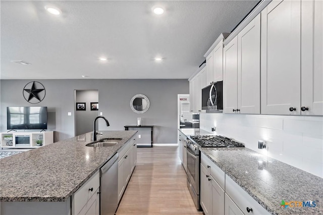 kitchen featuring a kitchen island with sink, a sink, decorative backsplash, baseboards, and appliances with stainless steel finishes
