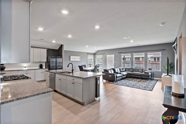 kitchen with a sink, stainless steel appliances, light wood-style floors, stone counters, and open floor plan