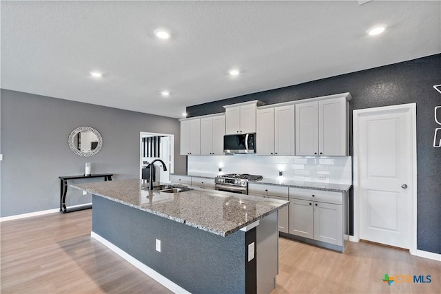 kitchen featuring light stone counters, light wood-style floors, appliances with stainless steel finishes, a sink, and a center island with sink