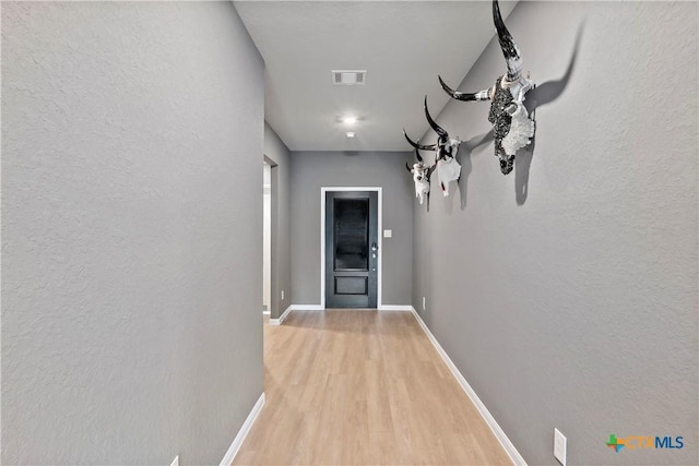 corridor featuring light wood finished floors, visible vents, a textured wall, and baseboards