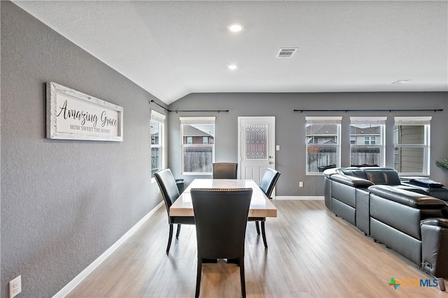 dining area with lofted ceiling, visible vents, a textured wall, light wood-style floors, and baseboards