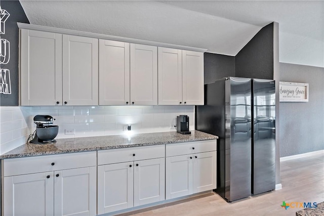kitchen featuring white cabinetry, light stone countertops, freestanding refrigerator, and backsplash