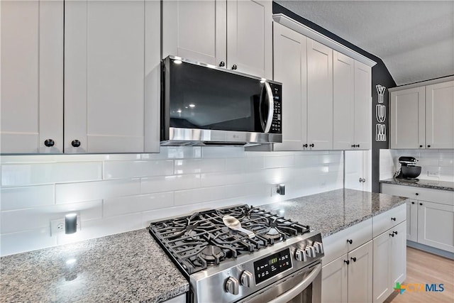 kitchen with light stone countertops, stainless steel appliances, backsplash, white cabinetry, and light wood-type flooring