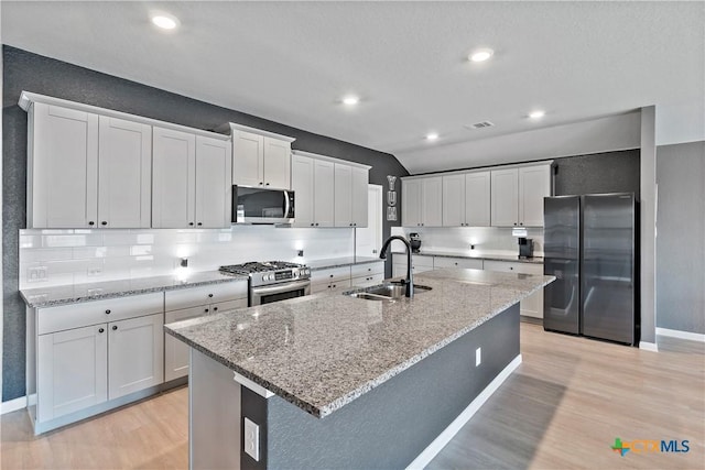 kitchen with tasteful backsplash, a sink, stainless steel appliances, light wood-type flooring, and a kitchen island with sink