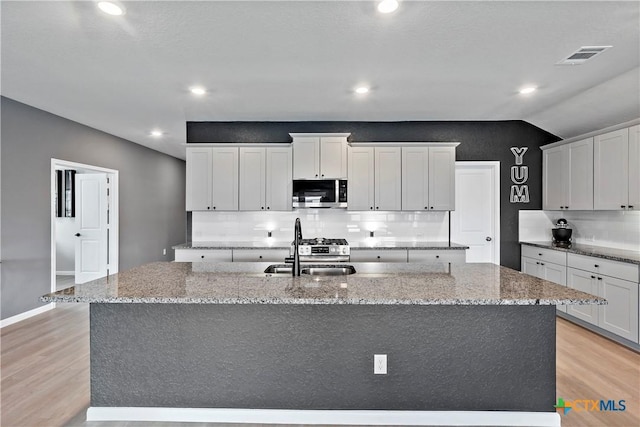 kitchen with stainless steel microwave, light wood-type flooring, decorative backsplash, and a sink