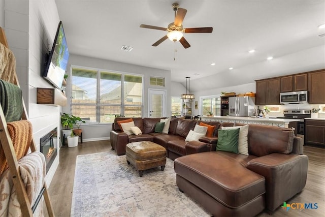 living room with ceiling fan, lofted ceiling, a fireplace, and light hardwood / wood-style flooring