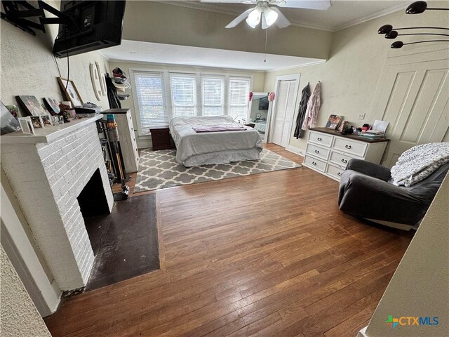 bedroom featuring dark wood-type flooring, ceiling fan, crown molding, and a fireplace