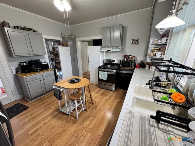 kitchen featuring gray cabinetry, stainless steel gas range oven, ornamental molding, pendant lighting, and light hardwood / wood-style floors