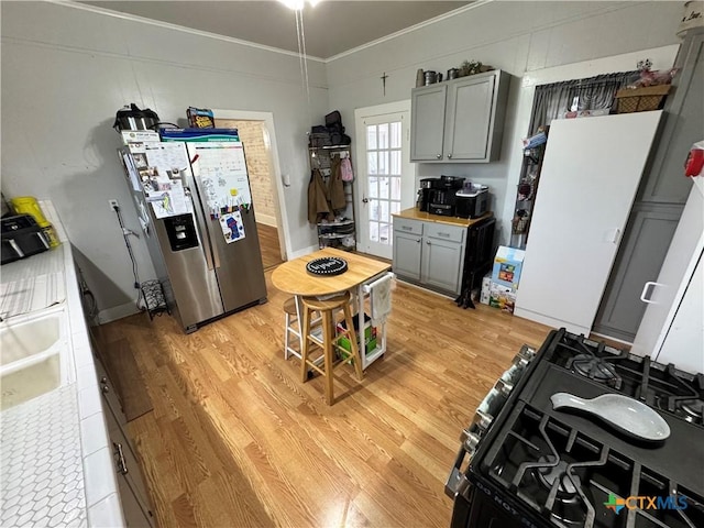 kitchen featuring crown molding, light hardwood / wood-style flooring, stainless steel fridge, gray cabinets, and gas range oven