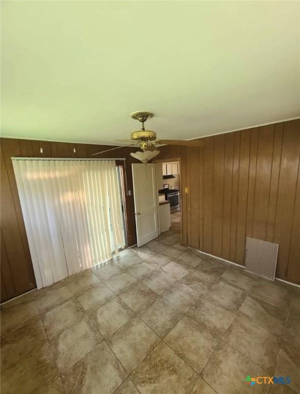 unfurnished living room with a ceiling fan and wood walls