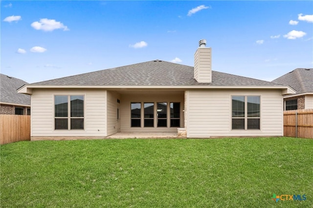 rear view of house with a lawn, a chimney, roof with shingles, fence, and a patio area