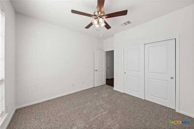 unfurnished bedroom featuring baseboards, visible vents, ceiling fan, carpet floors, and a closet