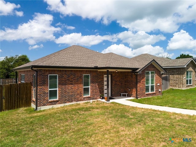 view of front of house with a shingled roof, a front yard, brick siding, and fence