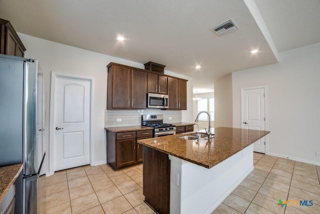 2241 Windswept Way, New Braunfels, TX 78132 - kitchen featuring appliances with stainless steel finishes, a sink, light tile patterned floors, a chandelier, and dark stone counters