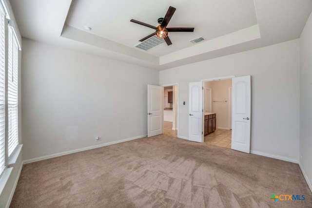 2241 Windswept Way, New Braunfels, TX 78132 - unfurnished bedroom featuring a tray ceiling, light colored carpet, baseboards, ensuite bath, and ceiling fan
