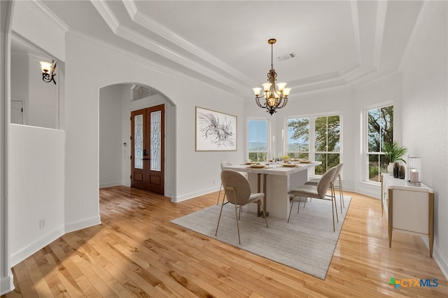 dining space with ornamental molding, light wood-type flooring, visible vents, arched walkways, and a raised ceiling
