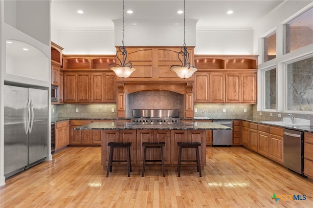kitchen featuring a center island, brown cabinets, a sink, stainless steel appliances, and crown molding