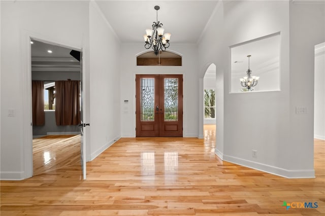 entrance foyer with french doors, crown molding, light wood-style flooring, arched walkways, and a notable chandelier