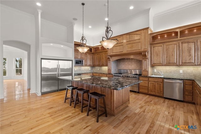 kitchen featuring a kitchen island, stainless steel appliances, brown cabinetry, and dark stone countertops