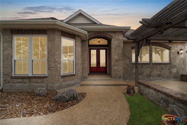 exterior entry at dusk featuring stone siding, a pergola, and french doors