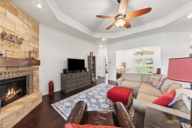 living room featuring ceiling fan with notable chandelier, a stone fireplace, crown molding, a tray ceiling, and dark hardwood / wood-style flooring