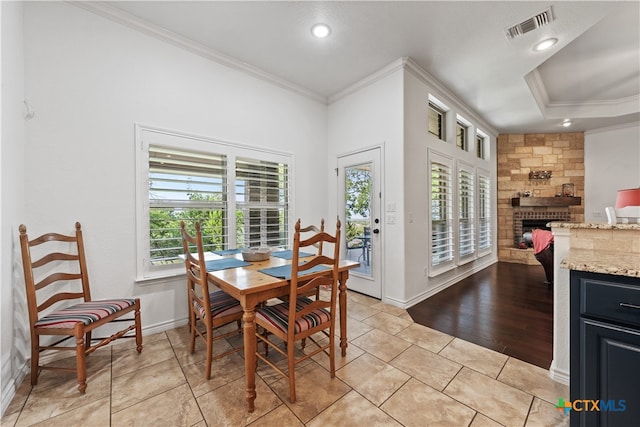 tiled dining space with a tray ceiling, a stone fireplace, and crown molding